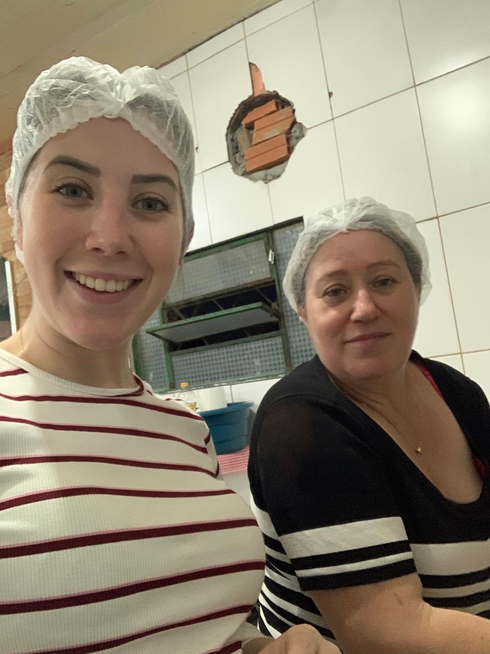 Débora jovem, de touca descartável, numa selfie com uma mulher mais velha na cozinha de casa